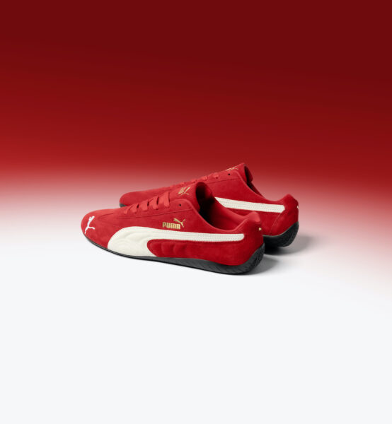 Czerwone buty Puma Speedcat, które mają białe akcenty oraz złoty napis, położone są na czerwono-białym tle.