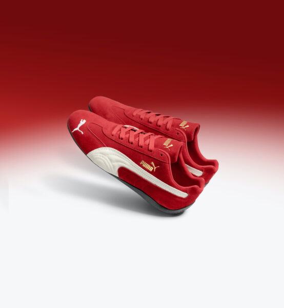 Czerwone buty Puma Speedcat, które mają białe akcenty oraz złoty napis, położone są na czerwono-białym tle.
