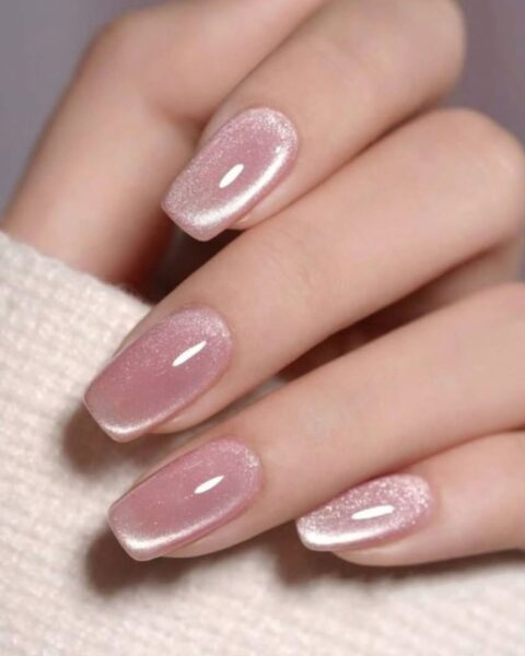 Zbliżenie na dłoń, która prezentuje manicure magnetyczny w kolorze różowym na długich, kwadratowych paznokciach.