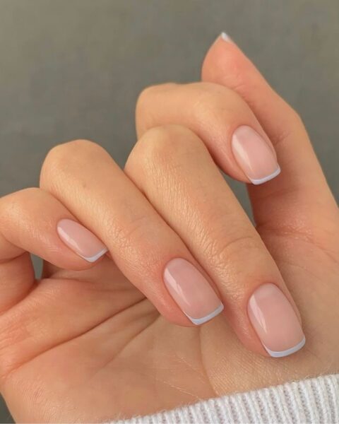 Zdjęcie dłoni ze zbliżeniem na paznokcie kwadratowe, średniej długości, ozdobione micro french manicure z bardzo cienką kreseczką przy brzegu.