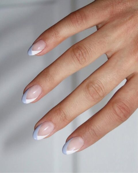 Zdjęcie dłoni ze zbliżeniem na owalne, średnie paznokcie z french manicure ale o prostych, graficznych kreskach w kolorze biało-niebieskim.