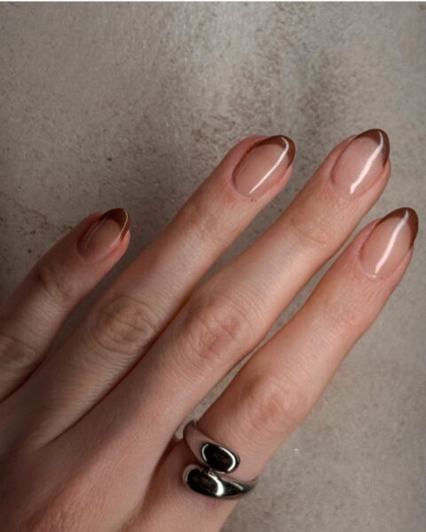 Zdjęcie ze zbliżeniem na długie, owalne paznokcie z kolorowym french manicure z brązową końcówką. Na palcu wskazującym widać srebrny pierścionek.