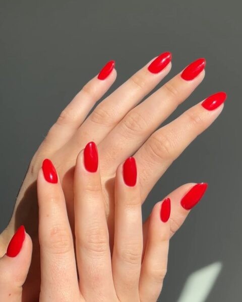 Zdjęcie dłoni z długimi, owalnymi paznokciami w kolorze czerwonym. Dłonie układają się tak, by prezentować manicure.