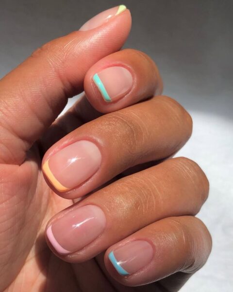 Zdjęcie dłoni i paznokci w stylu french manicure z pastelowymi, kolorowymi końcówkami.
