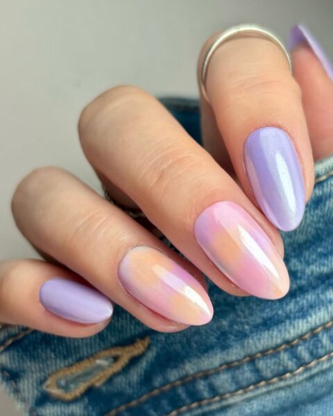 Zdjęcie dłoni ze zbliżeniem na kosmiczne pastele na paznokciach w stylu ombre nails, wykończone chromowanym pyłkiem. Paznokcie są długie i mają kształt migdała.