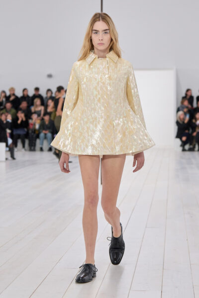 Modelka na wybiegu prezentuje ultramini sukienkę z długim rękawem w odcieniu butter yellow.
