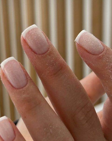 Zdjęcie dłoni ze zbliżeniem na paznokcie o krótkim, kwadratowym kształcie. Są pokryte specjalnym pyłkiem, który wykorzystuje się w manicure japońskim.