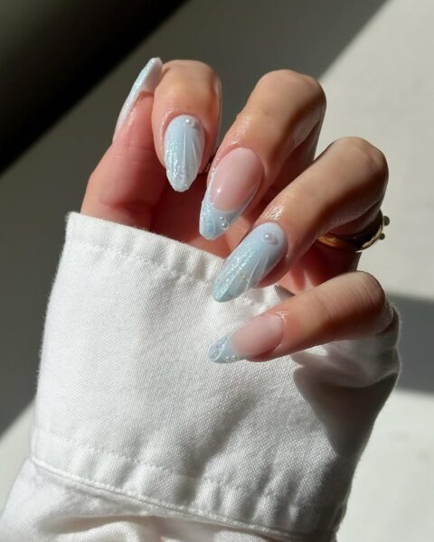 Zdjęcie dłoni z długimi, migdałowymi paznokciami pomalowanymi w stylu french manicure z błękitnym kolorem i strukturalnym wzorem muszelki. Dodatkowo paznokcie ozdobione są perełkami 3D.