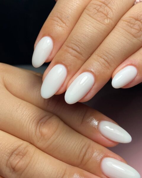 Zdjęcie dłoni z długimi, migdałowymi paznokciami w kolorze mlecznobiałym. Pozują tak, by prezentować manicure.