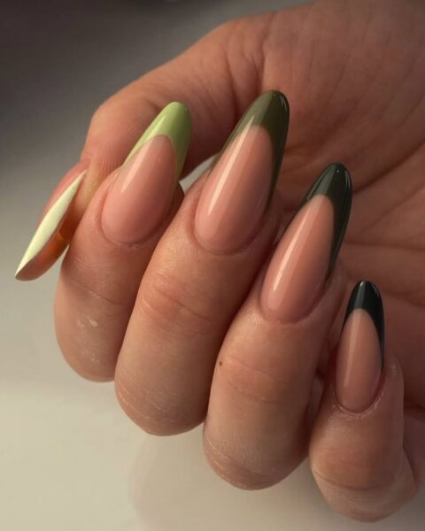 Zdjęcie dłoni ze zbliżeniem na długie, migdałowe paznokcie. Zdobi je manicure w kolorze dubajskiej czekolady, czyli czekoladowy beż oraz odcienie zieleni. Dłoń pozuje na białym blacie.