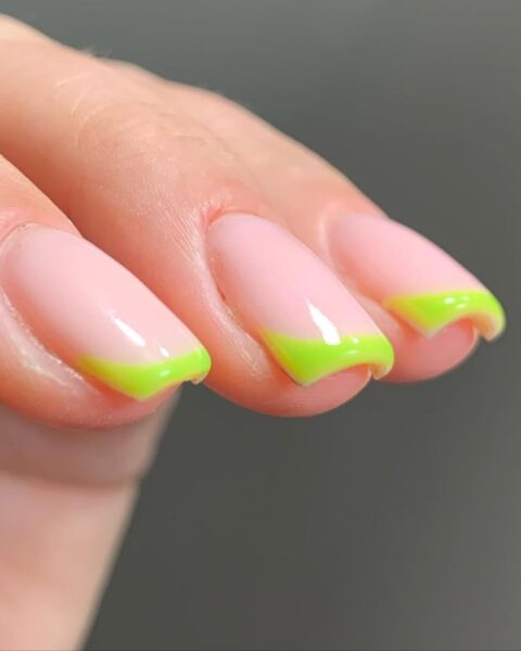 Zdjęcie dłoni z dużym zbliżeniem na kwadratowe paznokcie ze wzorem french manicure z zieloną końcówką.
