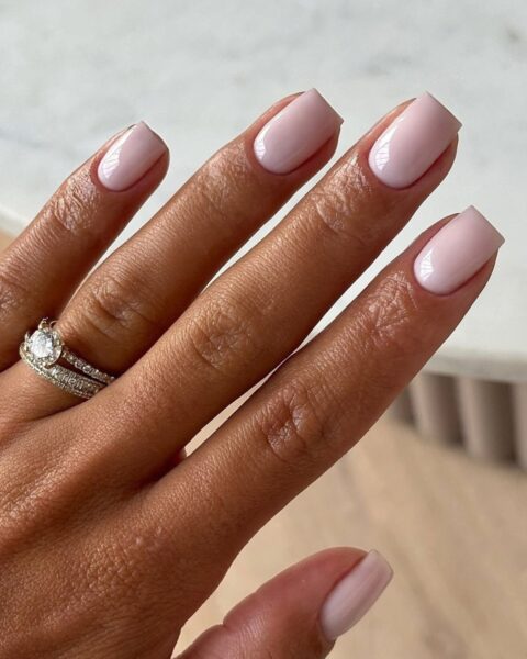 Zdjęcie dłoni z kwadratowymi, średniej długości panzokciami w neutralnym kolorze nude. Dłoń pozuje tak, by prezentować manicure.