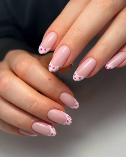 Zdjęcie dłoni ze zbliżeniem na paznokcie ze zdobieniem floral french manicure z kwiatkami przy brzegach. Dłonie pozują na tle białego blatu.
