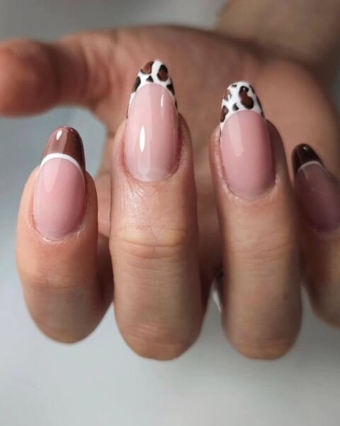 Zdjęcie dłoni ze zbliżeniem na długie, migdałowe paznokcie. Zdobi je wzór animal french manicure z końcówkami ze wzorem panterki. Dłoń pozuje na białym blacie.