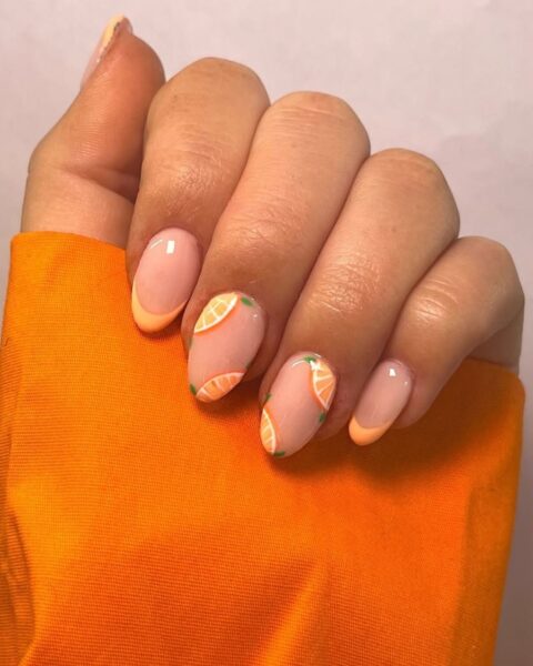 Zdjęcie dłoni z długimi, owalnymi paznokciami ze wzorem french manicure, ale na dwóch paznokciach jest drobny wzór pomarańczy.