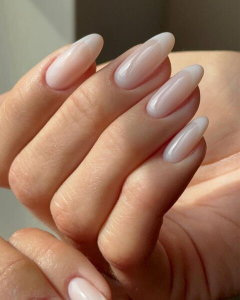 Zdjęcie dłoni ze zbliżeniem na długie, migdałowe paznokcie w stylu french manicure z mleczną bazą oraz perłowym wykończeniem.