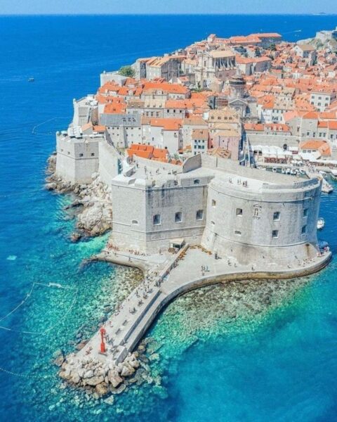 Zdjęcie z lotu ptaka na molo w mieście Dubrovnik w Chorwacji. Widać mury obronne oraz charakterystyczne czerwone dachy domów.