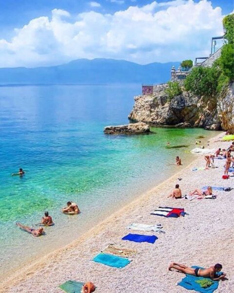 Zdjęcie plaży Sablićevo w Rijece. Widać niewielką plażę, lazurową wodę, skały, a także mnóstwo turystów.