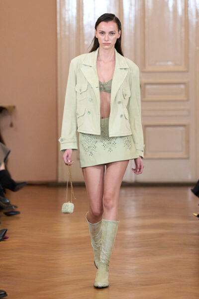Look od Ermanno Scervino: krótka pistacjowozielona spódniczka z perforowanym wzorem, dopasowana marynarka i botki – nowoczesna elegancja z letnim twistem.