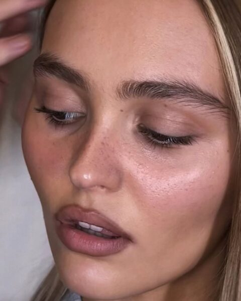 Zdjęcie ze zbliżeniem na twarz Lily Rose Depp w blond włosach, która ma makijaż no-make-up i usta obrysowane konturówką.