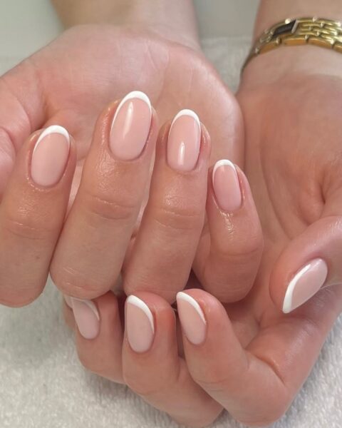 Zdjęcie dłoni ze zbliżeniem na paznokcie. Mają długi, owalny kształt i są pomalowane w stylu french manicure. Dłonie układają się tak, by prezentować manicure. Pozują na tle ręcznika, tuż po stylizacji.