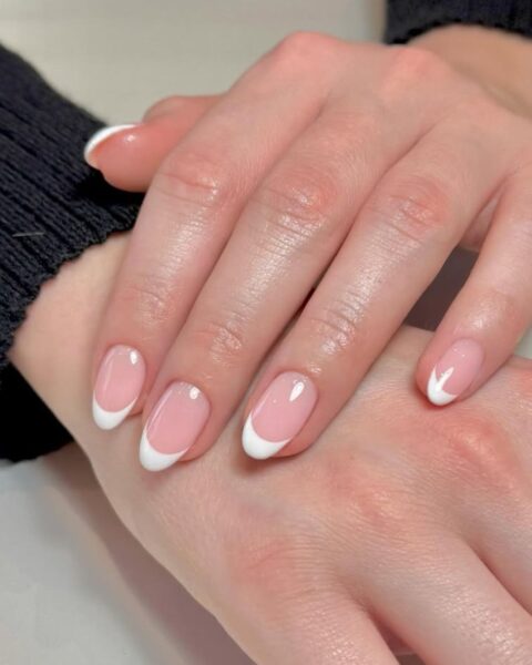 Zdjęcie dłoni ze zbliżeniem na długie, owalne paznokcie. Są pomalowane w stylu french manicure. Dłonie pozują na białym blacie i układają się tak, by prezentować manicure.