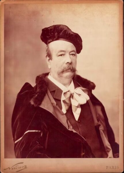 Portret Charles’a Fredericka Wortha, XIX-wiecznego projektanta mody, w eleganckim stroju z aksamitnym płaszczem z futrzanym kołnierzem i ozdobną kokardą pod szyją. Fotografia autorstwa Nadara, wykonana w Paryżu.
