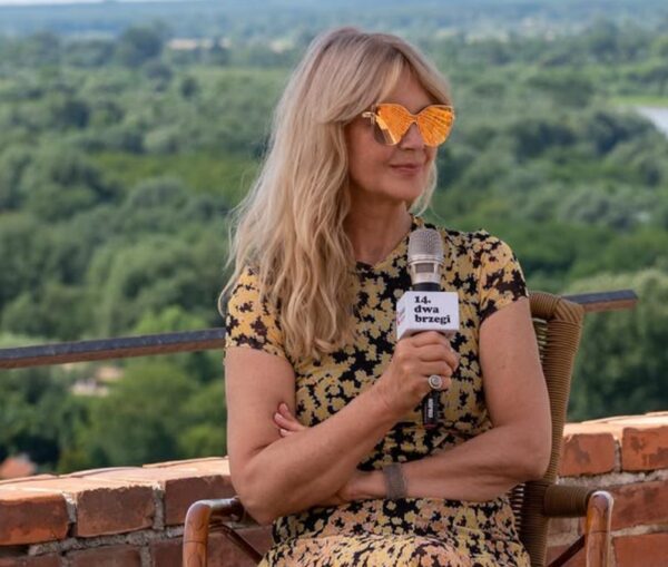 Grażyna Torbicka - prezenterka w kolorowej bluzce i w okularach przeciwsłonecznych, trzyma w ręce mikrofon.