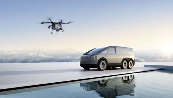 Futurystyczny pojazd elektryczny z sześcioma kołami stoi na platformie przy basenie, w tle ośnieżone góry. Nad pojazdem unosi się dron, a słońce zachodzi za horyzontem. Samochody XPENG.