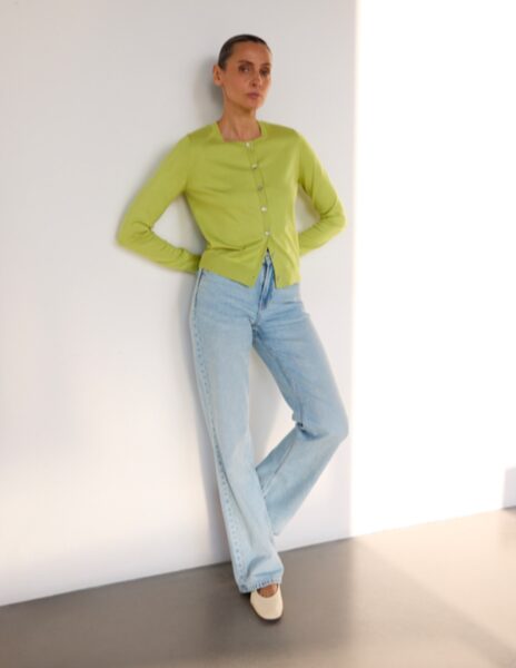 Kobieta w pistacjowym kardiganie z perłowymi guzikami, połączonym z jasnymi dżinsami – casualowy look inspirowany trendami kolorystycznymi lata 2025.