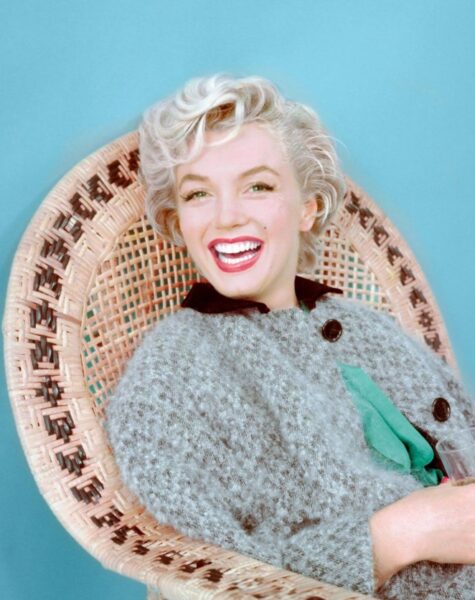 Marilyn Monroe siedzi na wiklinowym fotelu. Aktorka ubrana jest w szary sweter.