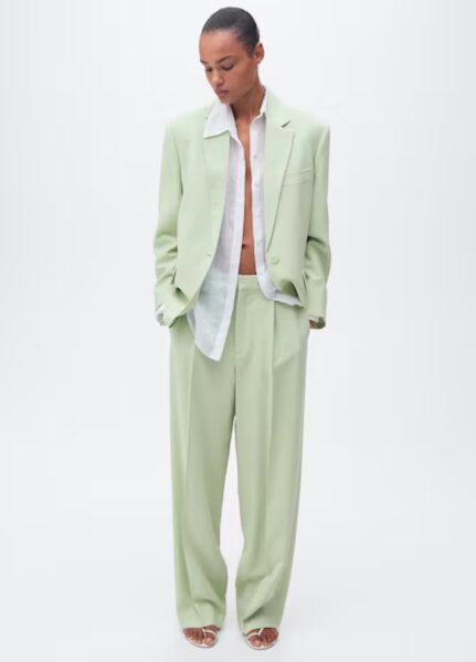 Modelka w luźnym, pistacjowozielonym garniturze z szerokimi spodniami i rozpiętą białą koszulą, tworzącym minimalistyczny i nowoczesny look.