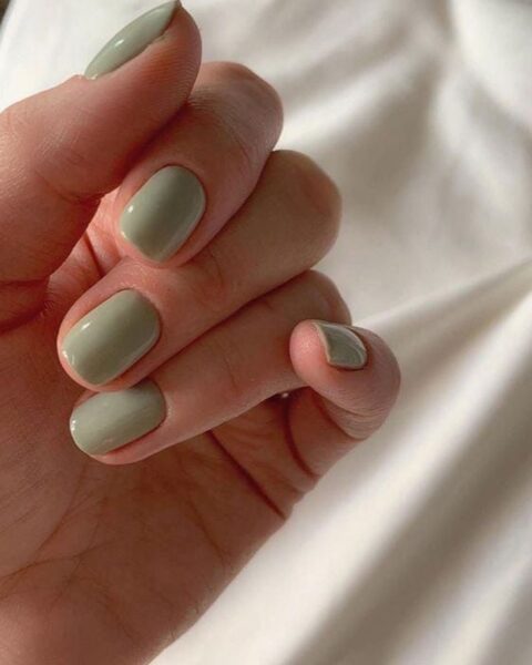 Najmodniejsze kolory manicure na lato 2025: na zdjęciu widać przykład szałwiowych paznokci o krótkim, owalnym kształcie. Dłoń pozuje na tle białego materiału.