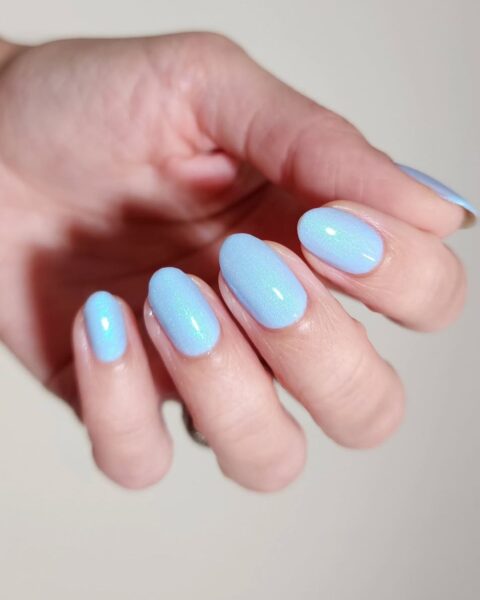 Zdjęcie dłoni ze zbliżeniem na długie, owalny paznokcie pomalowane na kolor jasnego błękitu w odcieniu baby blue.