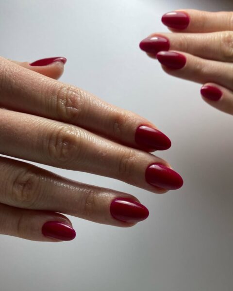 Zdjęcie dłoni z długimi, owalnymi paznokciami w kolorze ciemnej czerwieni na czerwiec 2025. Dłonie pozują tak, by prezentować manicure.