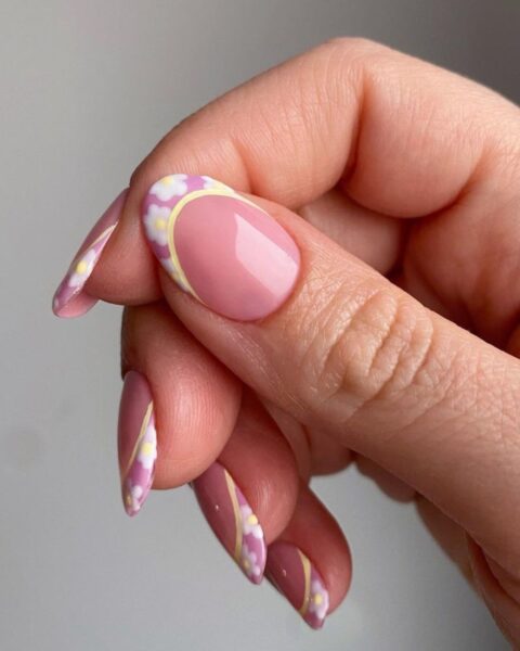 Zdjęcie dłoni ze zbliżeniem na kciuk. Widać owalny, długi paznokieć w stylu french manicure, ale z kwiatową końcówką.