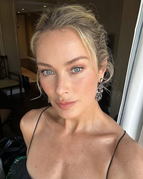 Zdjęcie dojrzałej kobiety. Robi sobie selfie z góry. Ma blond włosy spięte z tyłu, z kosmykami przy twarzy. Ubrana jest w czarny top na ramiączkach. W uszach wiszą długie kolczyki z kryształkami. Ma delikatny, letni makijaż.