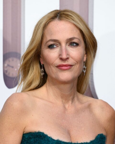 Zdjęcie aktorki Gillian Anderson, któa ma najpiękniejszy blond dla 60-latki, czyli karmelowy blond. Ubrana jest w zieloną sukienkę. W uszach ma wiszące kolczyki.