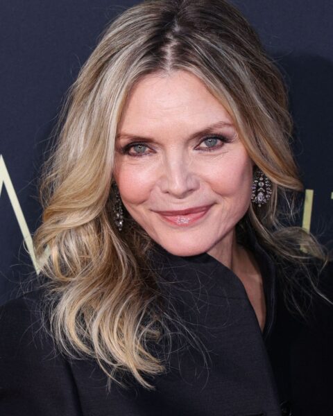 Zdjęcie aktorki Michelle Pfeiffer. Ubrana jest w czarną marynarkę i bluzkę. Ma długie, blond włosy w kolorze srebrnym, rozpuszczone na ramiona. W uszach ma wiszące kolczyki z kryształami.