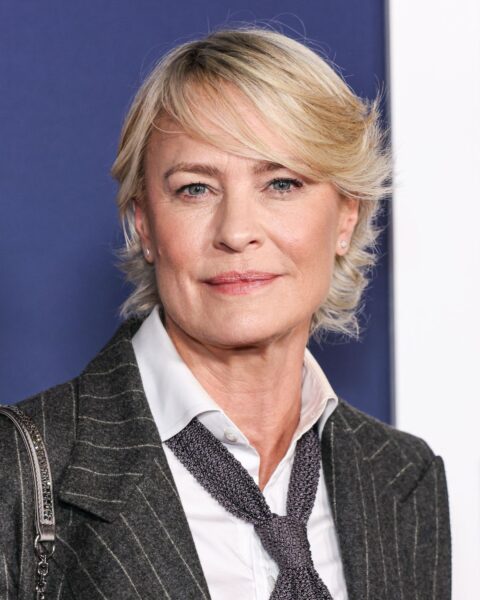 Zdjęcie aktorki Robin Wright. Ma krótkie włosy w kolorze blond, zaczesane na bok. Ubrana jest w czarny, prążkowany damski garnitur, białą koszulę oraz szary krawat.