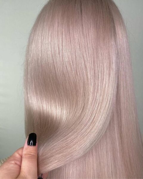 Zdjęcie modelki, jej włosów, dlatego stoi tyłem. Ma pastelowy blond z różowym podtonem, włosy są wygładzone, proste i mocno lśniące.