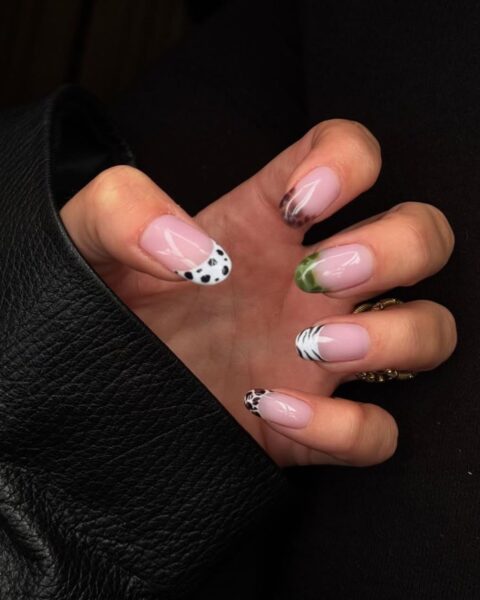 Zdjęcie dłoni ze zbliżeniem na długie, migdałowe paznokcie, które są pomalowane w stylu french manicure, ale zamiast białej końcówki mają wzory zwierzęce, z innym wzorem zwierzęcym na każdym paznokciu. Dłoń pozują tak, by prezentować manicure.