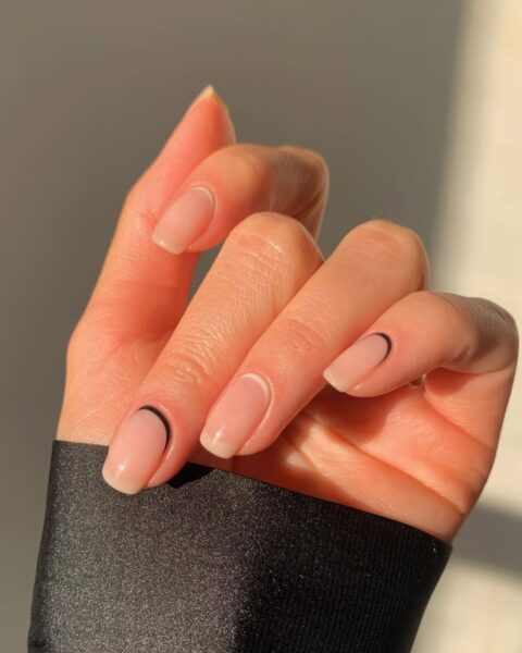 Zdjęcie dłoni ze zbliżeniem na długie, kwadratowe paznokcie z reverse french manicure w kolorze białym i czarnym.