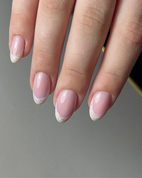 Zdjęcie dłoni z długimi, owalnymi paznokciami ze wzorem french manicure z perłową końcówką.