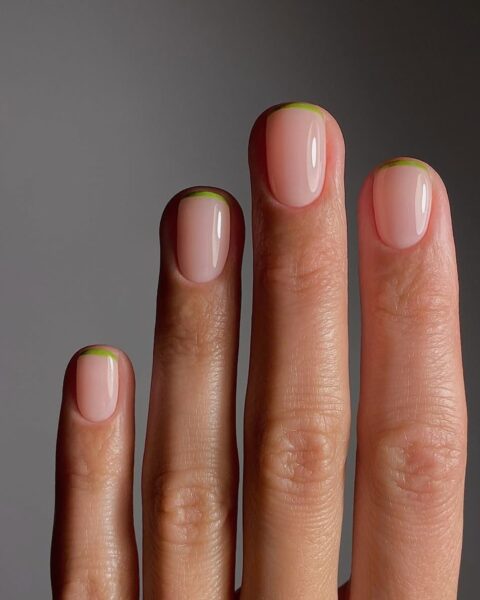 Zdjęcie dłoni ze zbliżeniem na krótkie, owalne paznokcie pomalowane w stylu french manicure, ale z zieloną, zamiast białą końcówką.