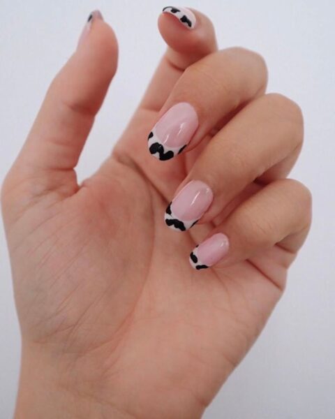 Zdjęcie dłoni z długimi, owalnymi paznokciami z french manicure ze wzorem krowich łat.