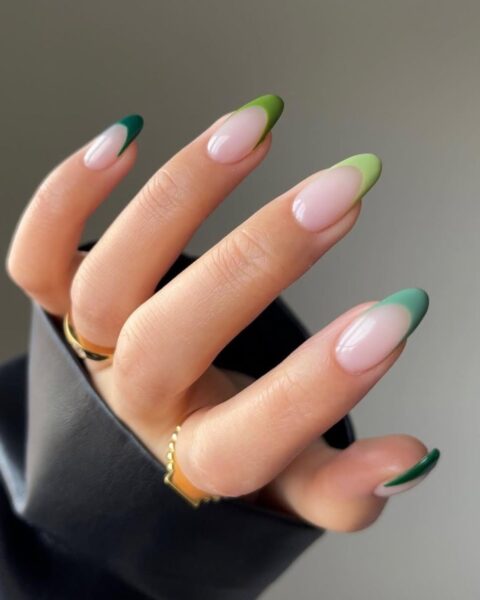 Zdjęcie ze zbliżeniem na pistacjowe i miętowe paznokcie pomalowane w stylu french manicure. Na palcach znajdują się dwa złote pierścionki.