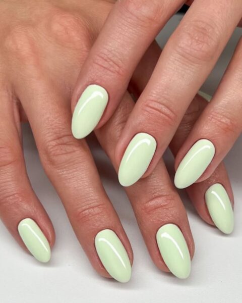 Zdjęcie dłoni z długimi, migdałowymi paznokciami w kolorze miętowym. Dłonie układają się tak, by prezentować manicure. Pozują na białym blacie.