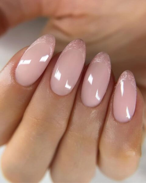 Zdjęcie dłoni ze zbliżeniem na długie, migdałowe, różowe paznokcie z perłową końcówką w stylu french manicure.