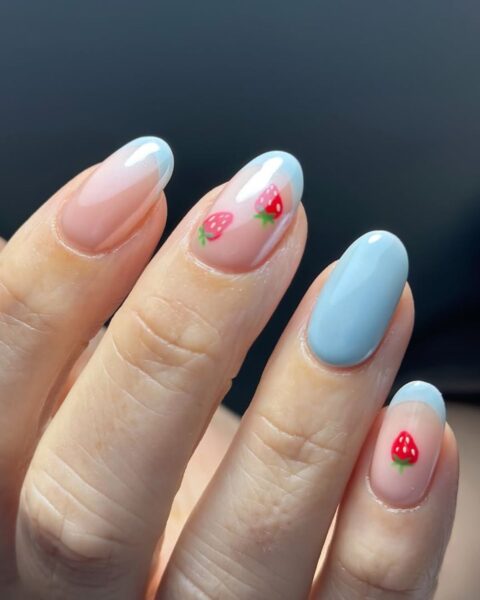 Zdjęcie dłoni ze zbliżeniem na długie, owalne paznokcie. Są pomalowane na niebieski french manicure i ozdobione wzorem truskawek.